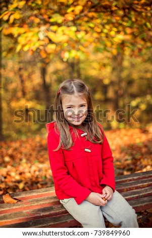Portrait child girl sitting on a wooden bench in a colorful autumn park. Vertical