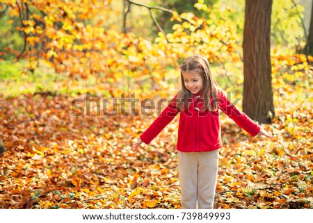 Little pretty girl 5-6 year in red jacket throws yellow leaves in autumn park or forest
