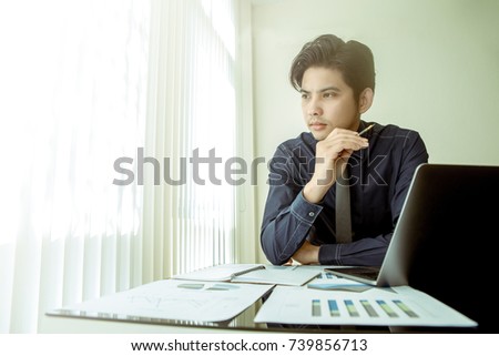 Asian businessman holding a pen touch his chin and look out the window for thinking.