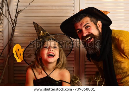 Halloween party and celebration concept. Wizard and little witch in hats. Father and daughter with Halloween decor. Girl and bearded man with cheerful faces on wooden door background