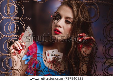 Young beautiful woman in a costume queen of hearts and make-up holds playing cards in their hands. background of creative decor and old rusty metal. Halloween. Preparation for a costume party.