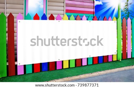 A white banner mounted on a wooden fence painted with paints of different colors