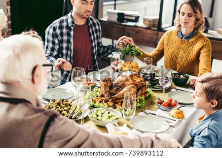 family holding hands and praying on thanksgiving before holiday dinner