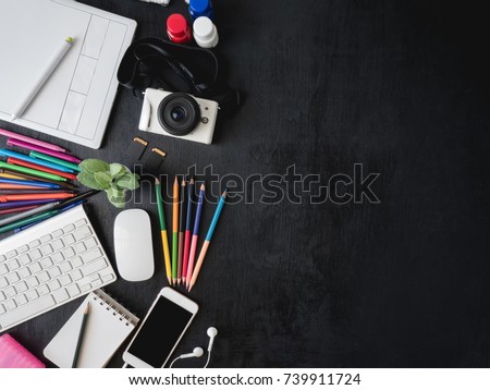 top view of graphic designer table with graphic tablet, smartphone, mouse, keyboard and other accessories on black wooden background with copy space, creative designs concept.