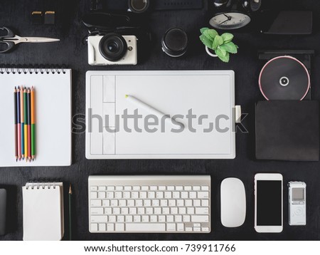 top view of graphic designer table with graphic tablet, smartphone, mouse, keyboard and other accessories on black wooden background, creative designs concept.