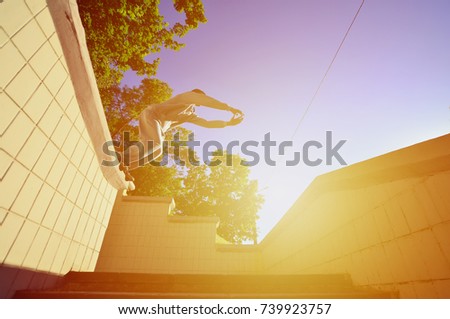 A young guy performs a jump through the space between the concrete parapets. The athlete practices parkour, training in street conditions. Bottom view
