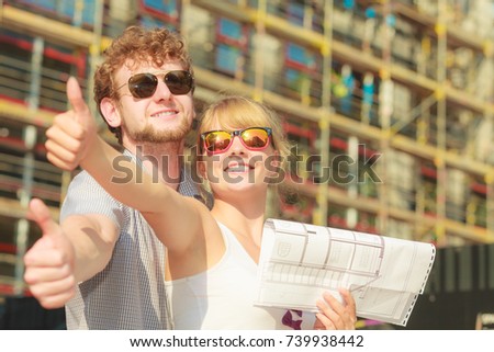 Real estate and family concept - young couple on front of new big modern house with blueprint project dreaming about home showing thumb up sign