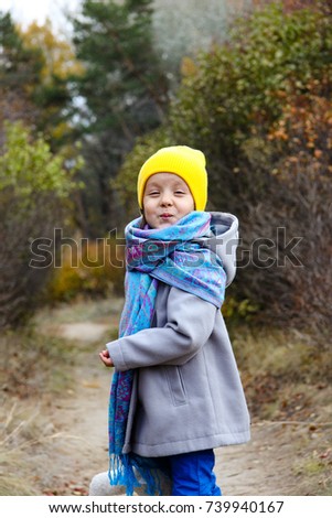 the little girl in the yellow hat in the autumn Park building faces and sends a kiss