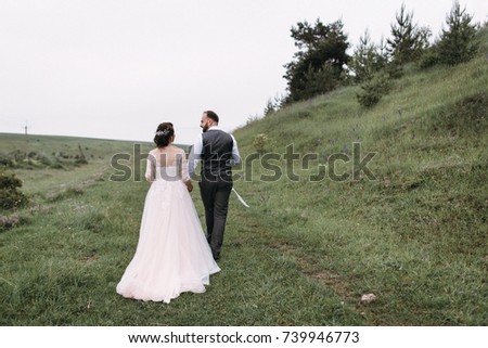 Bride's wedding walk in a luxurious dress with the groom with a beard near the forest on the grass with flowers. Happy wedding. Wedding day. Holding hands and hugging