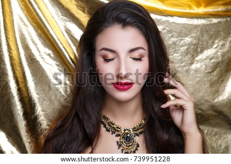 Beautiful woman wearing massive necklace. Long black wavy hair. Professional cosmetics makeup. Dark red lipstick lip-gloss. New photo close up portrait, shiny gold color background horizontal banner