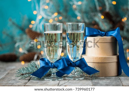 Two champagne glass on christmas bokeh with snow,lights,fir and gift boxes on blue background