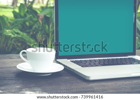 Conceptual green workspace, Laptop with blank screen on table, coffee cup and green garden background
