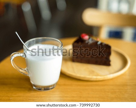 glass of milk with chocolate cakes on top red cherry background in wooden plate on wood table