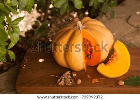  Pumpkin lies on a wooden board, next to green leaves, nuts, seeds, spices and pumpkin slice.Preparation for Halloween party