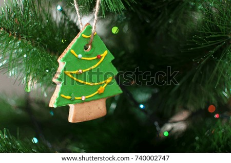 Cookie in the form of a Christmas tree is hanging on a branch of Christmas tree. Selective focus, bokeh. Holiday background or image.