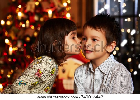 Children near Christmas tree. Girl kissing boy.