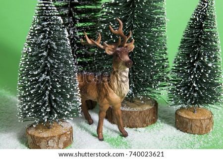 Isolated group of full artificial firs like a small snowy forest tree with a figurine reindeer inside on a vibrant red background. Minimal still life photography