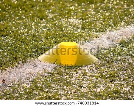 Bright yellow plastic cone on white soccer line. Plastic football green turf playground with grind black rubber in core. 
