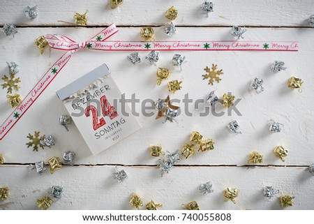 tear-off calendar with 24th of december (in German) on top, many decorative presents around on a wooden surface