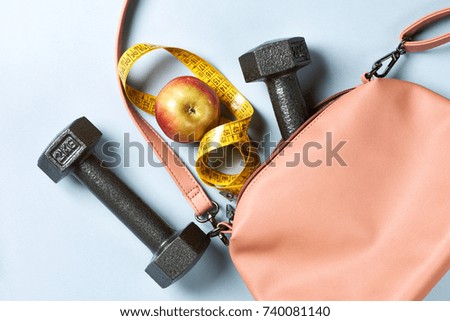 Pink leather ladies handbag with dumbbell, apple and centimeter on blue background