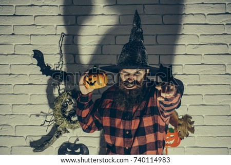 Halloween jack o lantern. Holiday celebration symbols on brick wall. Hipster with angry face in witch hat and plaid shirt. Mystery and horror concept. Man with pumpkin pointing finger in dark shadow.