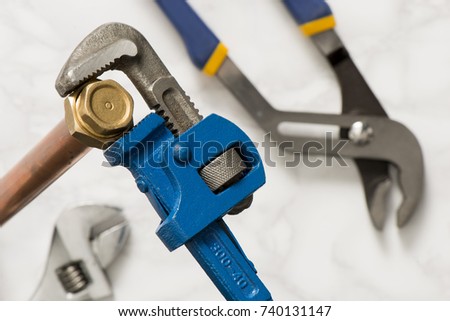 Pipe wrench clamping on a brass nut with grip and adjustable spanner in the background