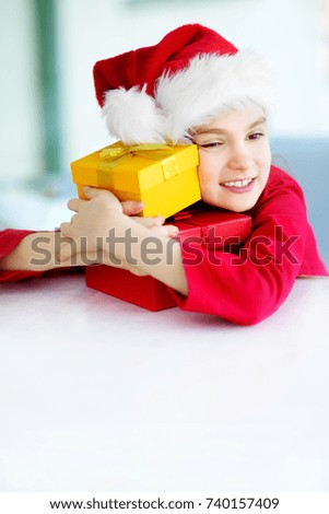 Adorable little girl wearing Santa hat opening a giftbox on Christmas morning. Celebrating Xmas at home.