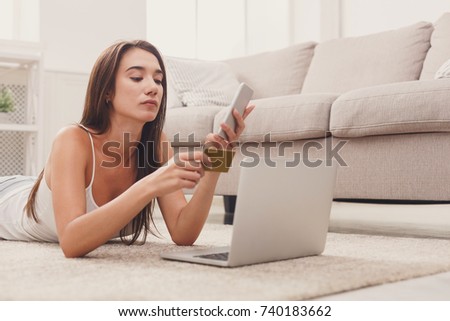 Pensive woman shopping online with credit card and laptop, lying on floor, thinking what to buy, copy space