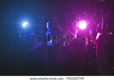 Happy friends celebrating new year at night club. Classy people enjoying life, dancing, drinking champagne and having fun at dark smoky background, showered with confetti. Christmas party background