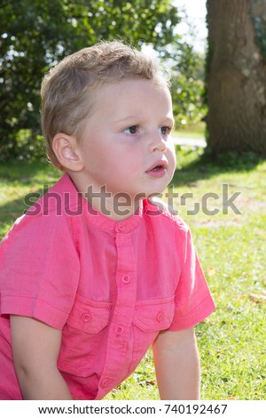 Spring or summer portrait of cute young boy playing with flower outdoors in clover field