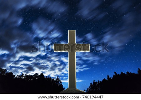 Wooden Christian cross standing under a fast moving cloud sky at night, backlit by white. Symbol of Jesus and worship background