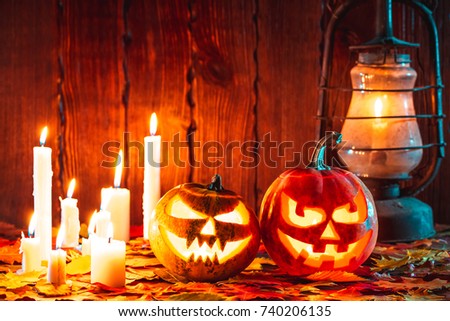 Halloween pumpkin with glowing face on a wooden background with many flaming candles, an antique lantern and autumn leaves. Idea for flyers, poster, placard, billboard
