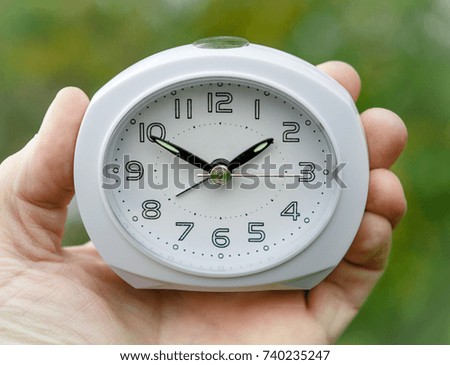 Hand holding white alarm clock.