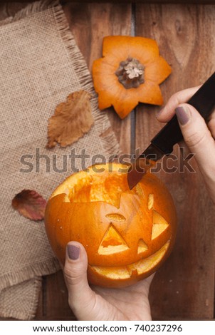 wooden table. and the hands hold a pumpkin with a picture for Halloween.