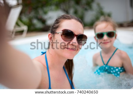 Happy mother and her adorable little daughter at outdoors swimming pool taking selfie on tropical vacation