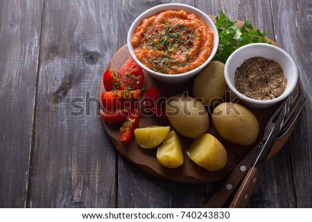 Young potatoes boiled in a peel with zucchini caviar or dip of vegetables, spices, fresh tomatoes and parsley on a wooden board, free space. Simple healthy homemade food