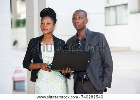 portrait of a businessman and a businesswoman standing near a pillar of a business center and working with a laptop.