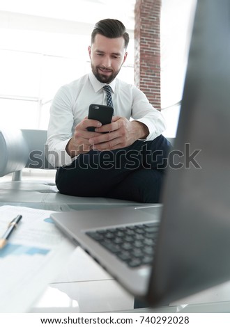 Businessman looking at screen smartphone sitting in front of an open laptop