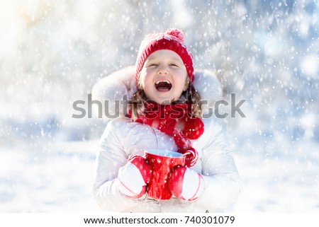 Child drinking hot chocolate with marshmallows in snowy winter park. Kid with cup of warm cocoa drink on Christmas vacation. Little girl playing in snow on Xmas eve. Family outdoor winter fun.