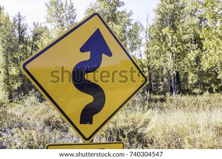 Winding road warning sign in front of a background including nature