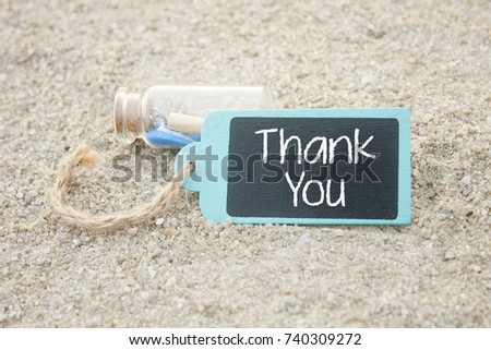mini bottle and wooden tag written thank you over sand background