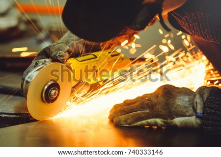  man in ordinary clothes and protective glasses with angle grinders while working in the workshop cutting metal Royalty-Free Stock Photo #740333146