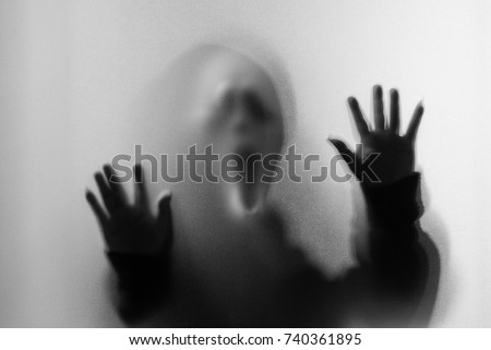 Shadow blur of horror man in screaming mask and hand touches the glass.Dangerous man behind the frosted glass.Mystery man.Black and white picture.Blur picture.Add effects noise and grain.Halloween.