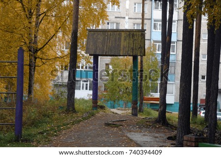 Decorative wooden gazebo with a roof, turquoise and violet, park with pine and birch, yellow and green leaves, needles. Playground. Autumn background