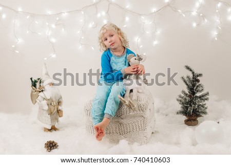 Portrait of blonde Caucasian child girl with blue eyes sitting with toys celebrating Christmas or New Year holiday