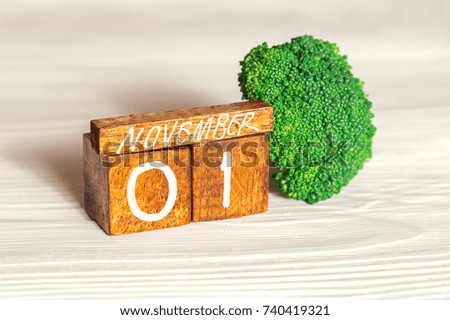 November 1st on wooden calendar and broccoli on light  background. Vegan day
