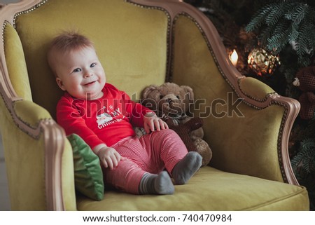 Little cute boy in red pullover smile while sitting in old-fashioned armchair near christmas tree in room. Close up shot
