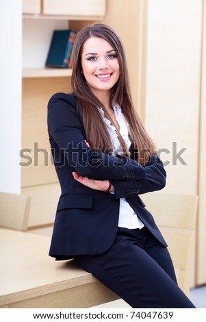 Young happy businesswoman in suit standing near the table in the office