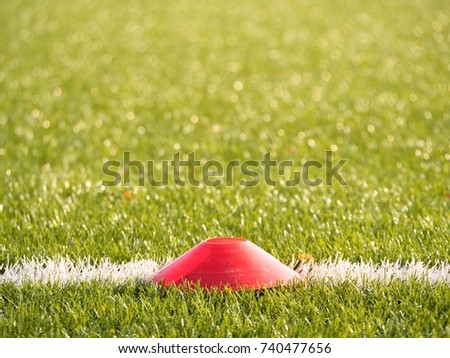 Bright red plastic cone on painted white line of soccer field. Plastic football green turf playground with grind black rubber in core. 