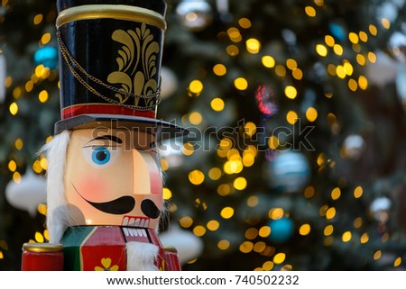 Close-up detail of a wooden nutcracker statue with a defocused background of glowing Christmas tree lights and ornaments. Singapore. Travel and celebration concept.